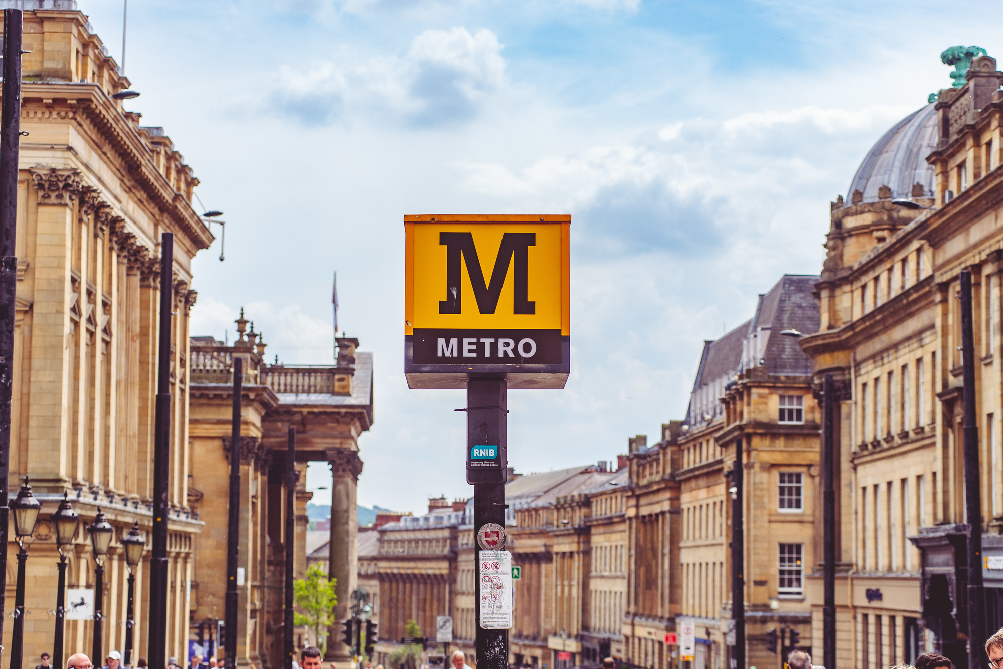 The Metro sign for monument station, framed by the honey-stone facades of Grey